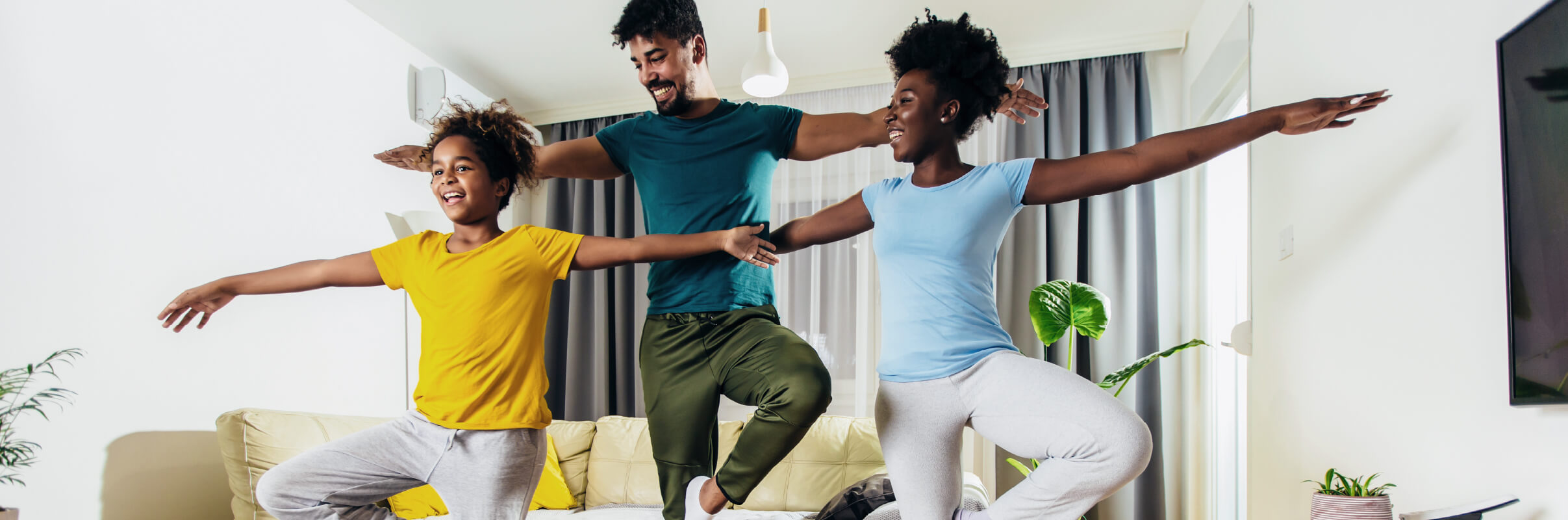 Family of three doing yoga in family room, smiling